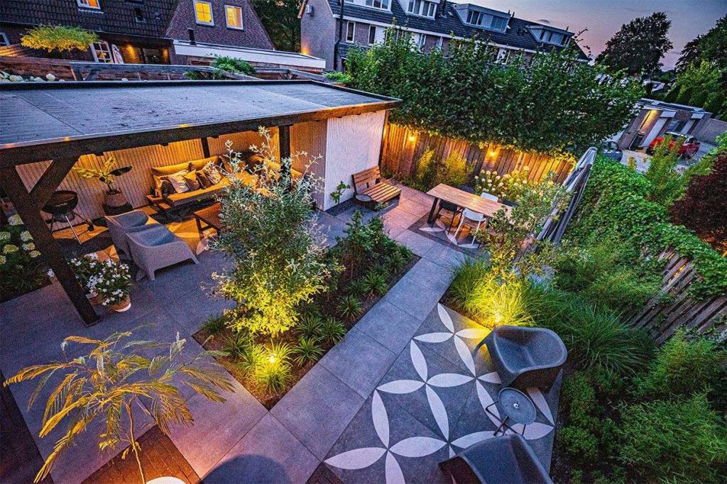 Verlichte tuin met terras, beplanting en overkapping in de avond