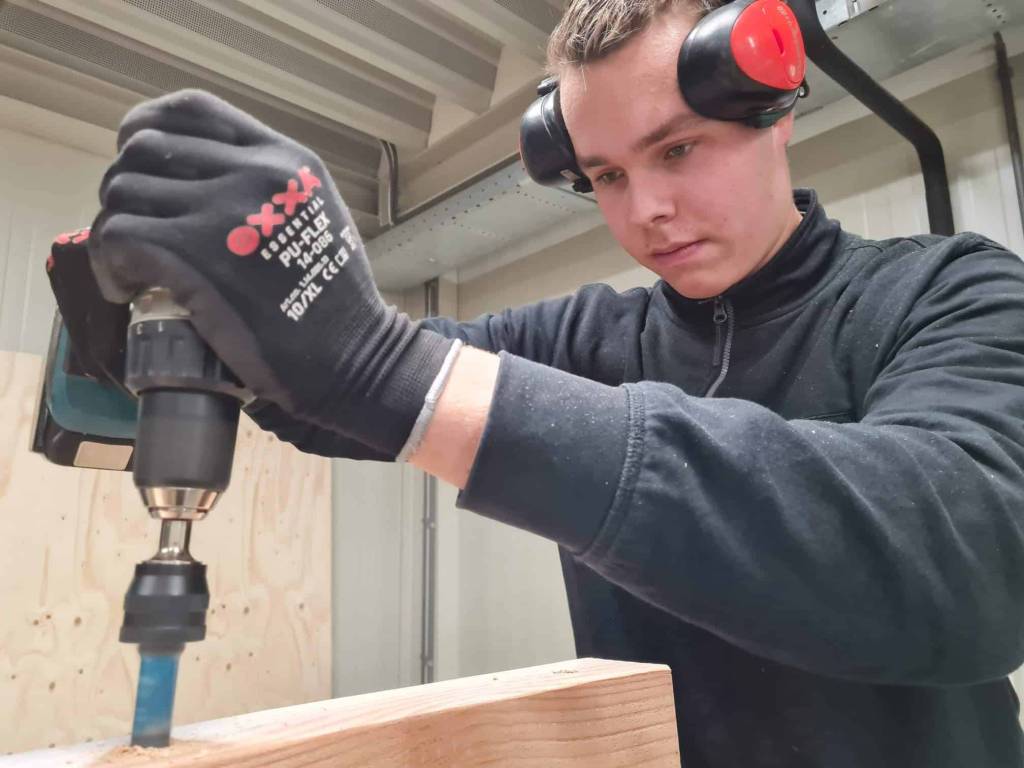 Medewerker met gehoorbescherming boort in hout