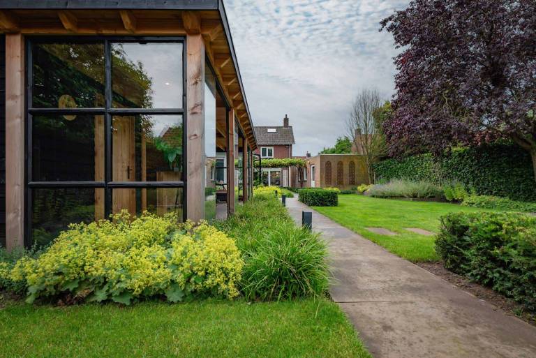 Groene en geelgroene borders langs een houten tuinpaviljoen