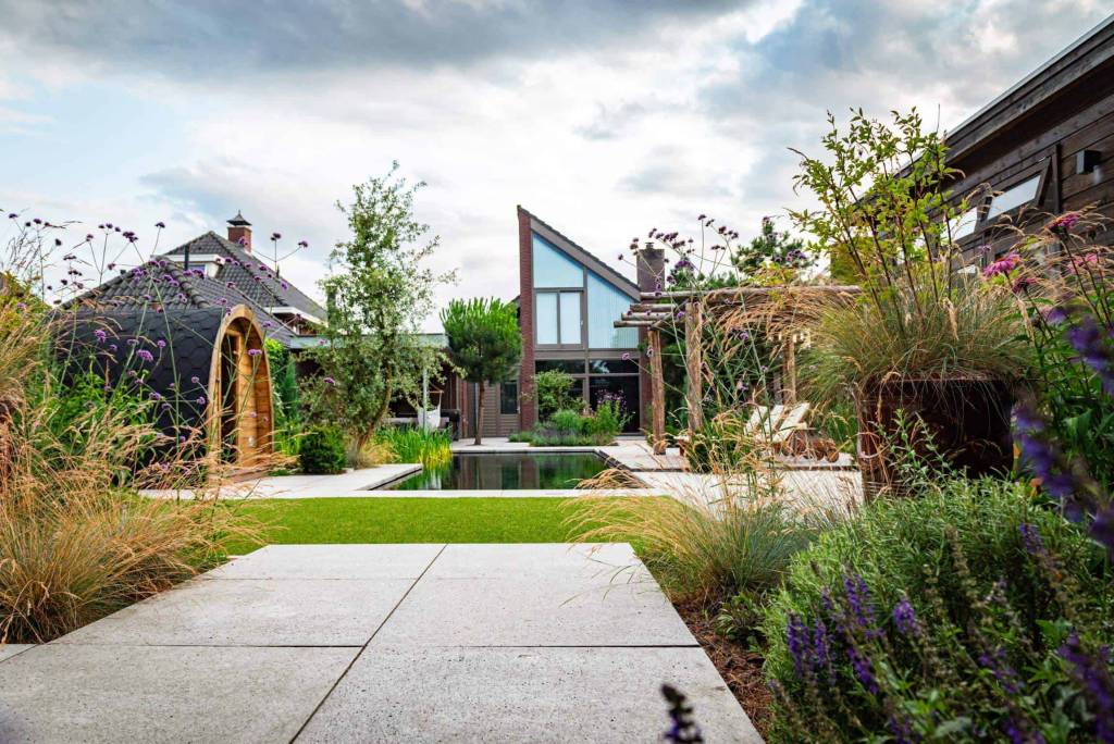 Breed tuinpad met gazon, borders en een glazen tuinpaviljoen