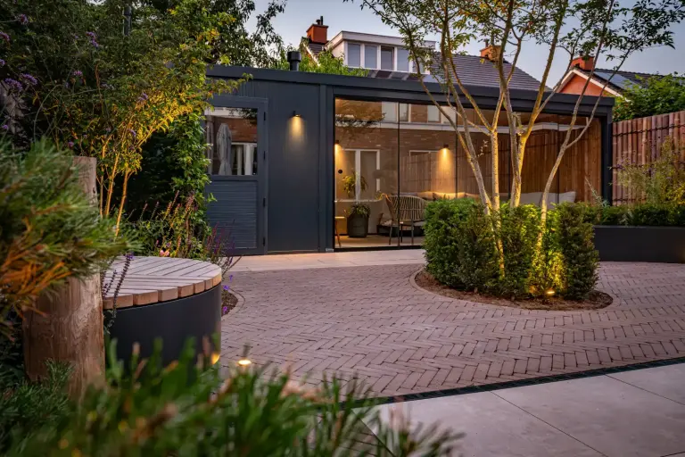 Glazen tuinpaviljoen naast verlichte groene borders